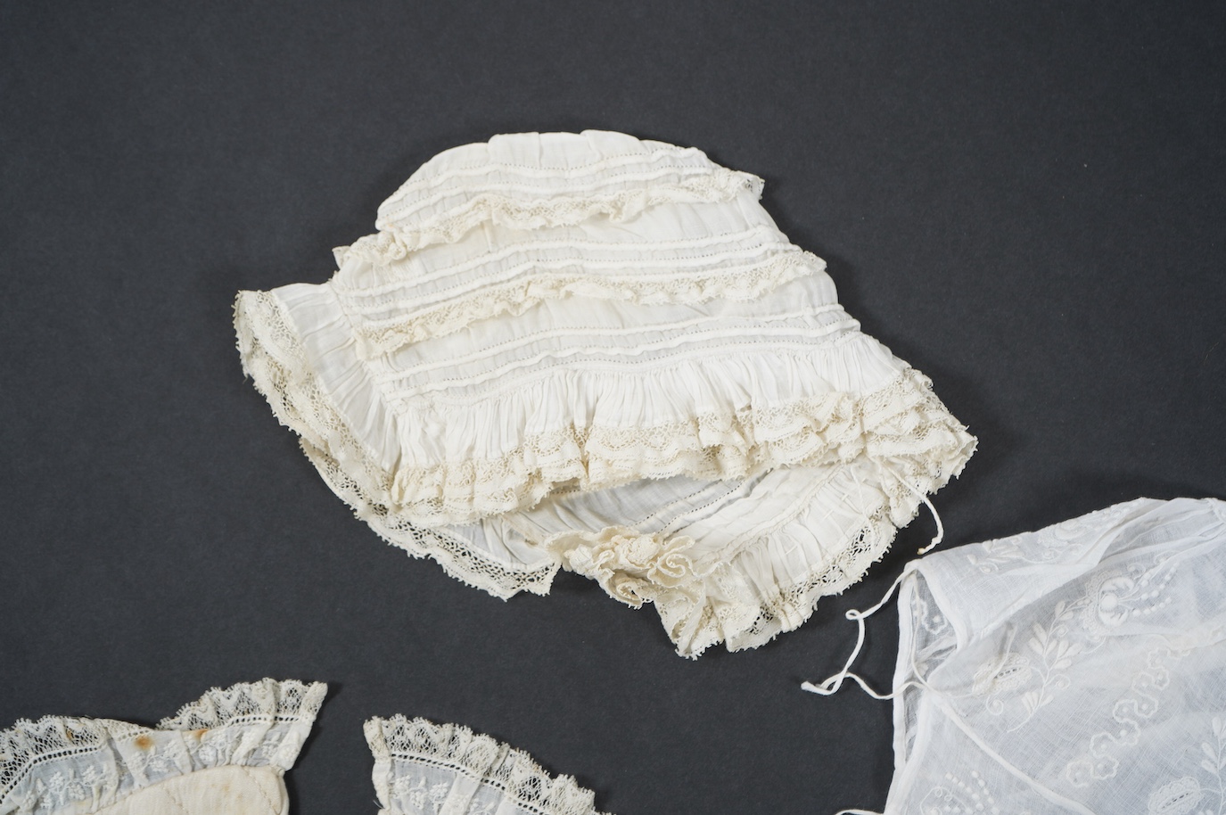 An 18th century Holly Point needle lace panelled linen baby bonnet, an early 19th century white worked baby bib and bonnet and a later 19th century finely ruffed lace bonnet (4). Condition - Holly Point bonnet and bib ha